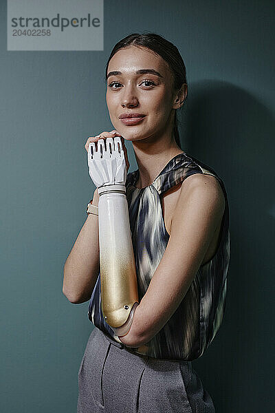 Smiling woman with bionic arm standing in front of green wall