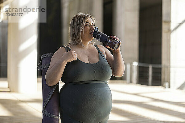 Curvy young woman drinking water through bottle