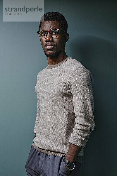 Confident young man with hands in pockets leaning on green wall