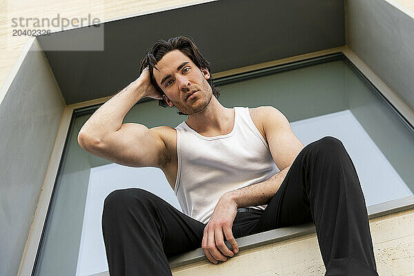 Handsome young man with hand in hair sitting on window