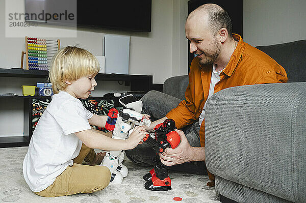 Son and father playing with robots sitting on floor at home