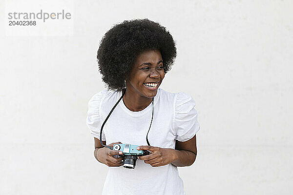 Cheerful young Afro woman with camera against white background