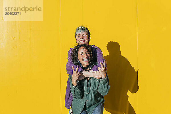 Playful lesbian couple embracing in front of yellow wall