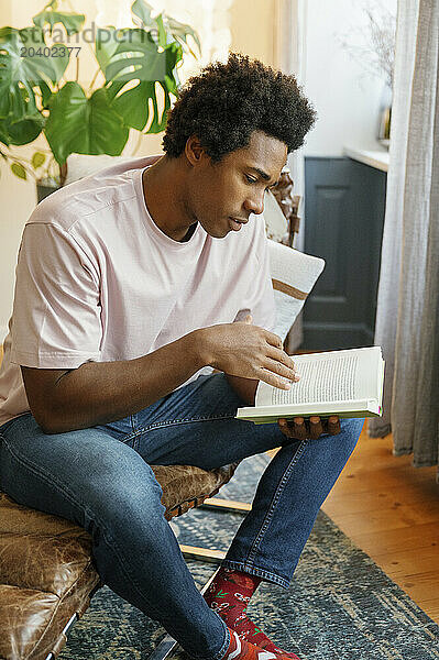 Man reading book sitting on lounge chair at home