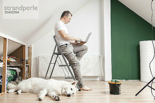 Man using laptop with dog resting on floor at home