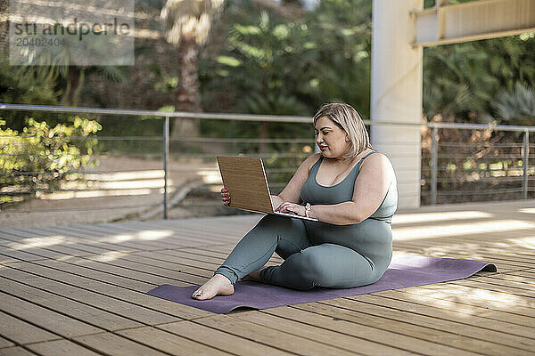 Young curvy woman using laptop on footbridge in park