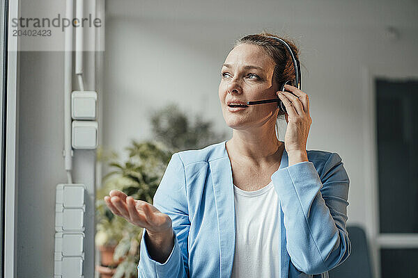 Confident mature businesswoman talking through headset in office