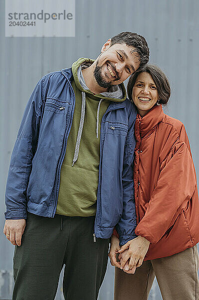 Happy couple holding hands and standing in front of corrugated iron