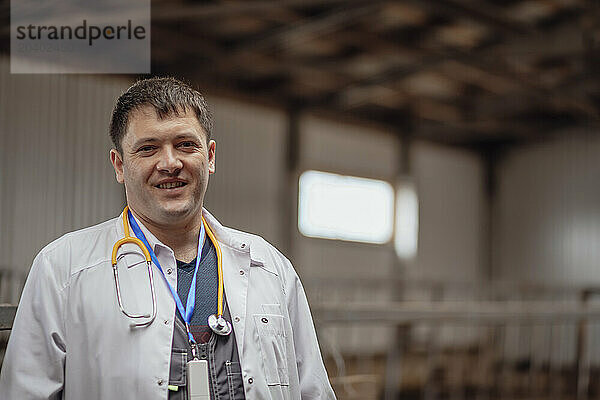 Smiling veterinarian wearing lab coat and standing at farm