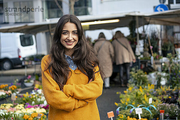 Smiling woman standing with arms crossed at flower market