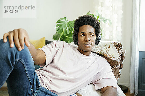 Man listening to music through wireless headphones on lounge chair at home