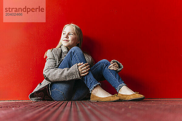 Smiling girl sitting on floor near red wall