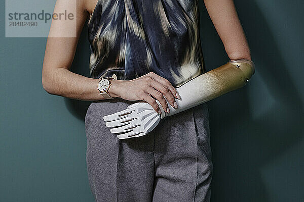 Young woman with bionic arm standing in front of on green wall