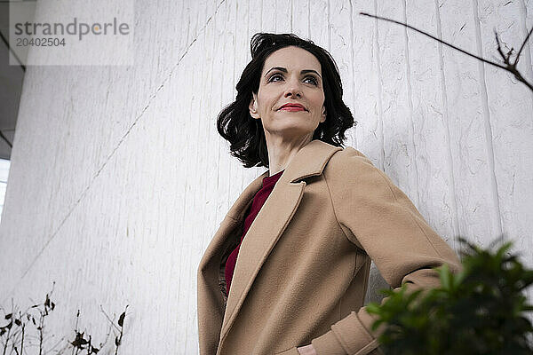 Businesswoman in trench coat leaning on wall