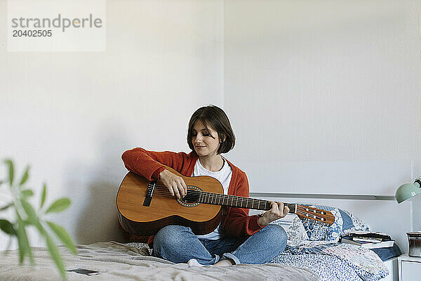 Beautiful woman practicing guitar sitting on bed at home