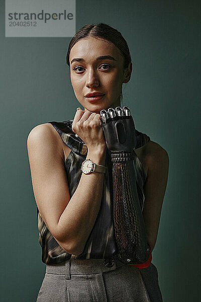 Confident woman with black bionic hand standing in front of green wall