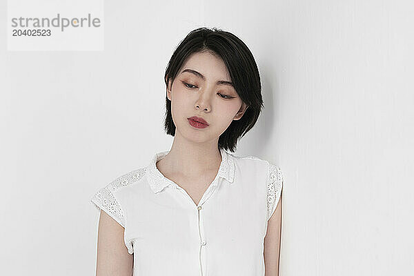 Thoughtful woman in white dress leaning on white backdrop