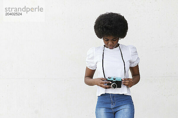 Young Afro woman standing with camera against white background