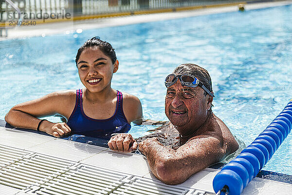 Senior man with young woman leaning at poolside on sunny day