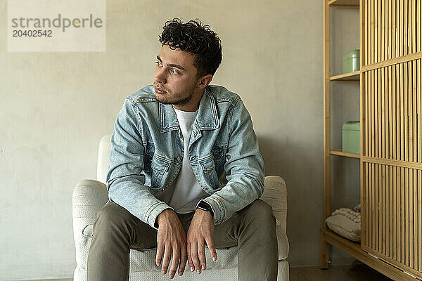 Thoughtful man sitting on armchair at home