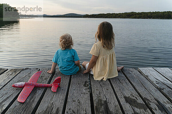 Brother and sister sitting on pier over lake