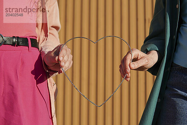 Lesbian couple holding metal heart shape on sunny day