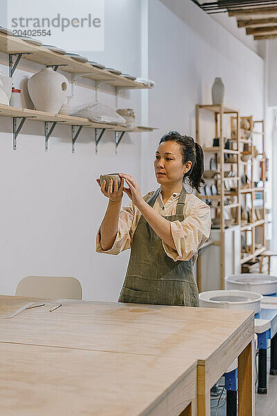 Artist molding shape on clay standing by table in pottery studio