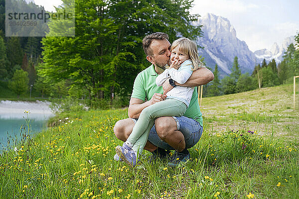 Father kissing daughter and crouching on grass