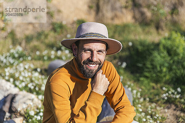 Smiling man wearing hat and sitting on sunny day