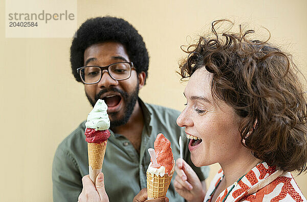 Happy friends sharing ice cream in front of wall