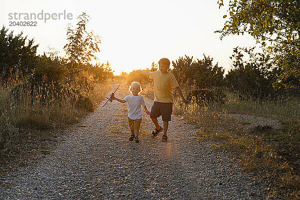 Brothers playing with toy airplane walking on footpath at sunset