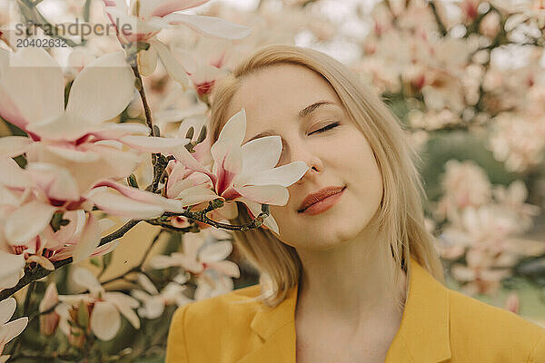 Blond woman with eyes closed by blossoming magnolia tree in garden