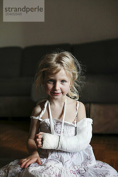 Girl with broken arm sitting on floor at home