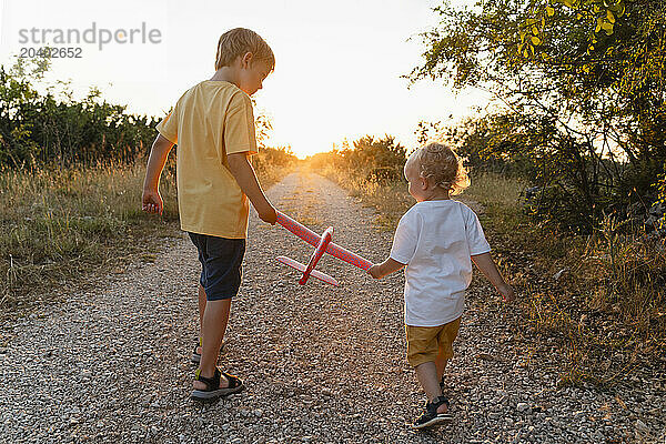 Brothers with toy airplane walking on footpath at sunset