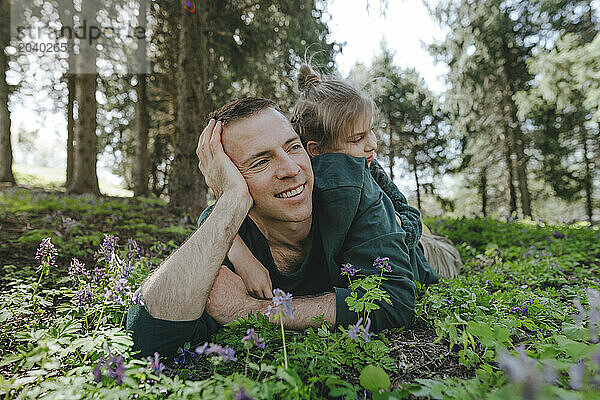 Girl lying on smiling father over green grass in forest