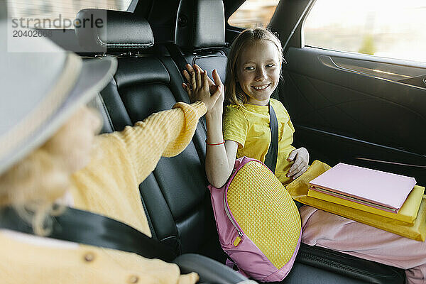 Happy sisters giving high-five sitting in backseat of car