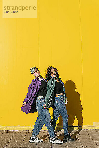 Lesbian couple posing together in front of yellow wall