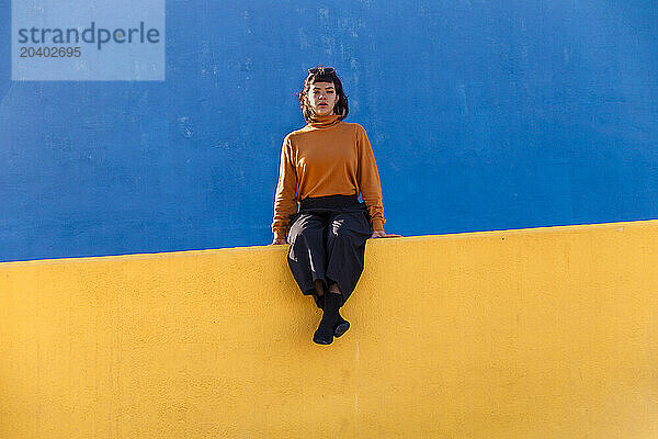 Young woman sitting on yellow wall