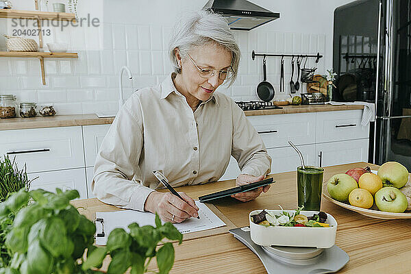 Woman planning menu using tablet PC in kitchen at home