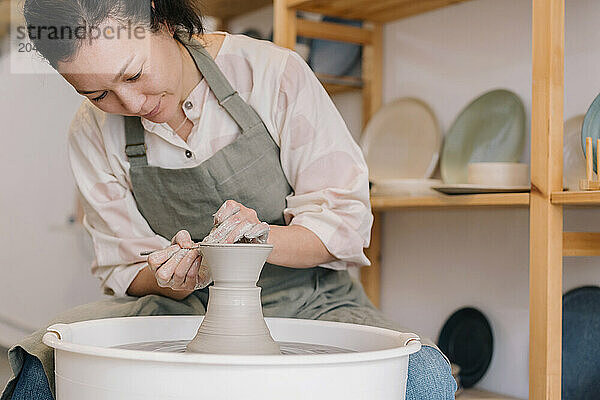 Confident craftsperson molding clay on pottery wheel at workshop