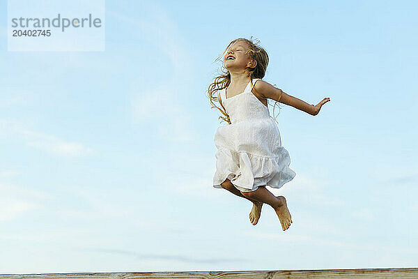 Cheerful girl jumping under sky