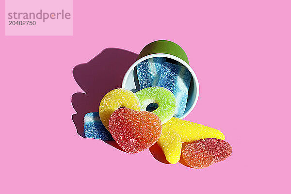 Jelly candies lying with cup over pink background