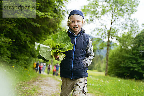 Smiling boy with leaves walking in forest