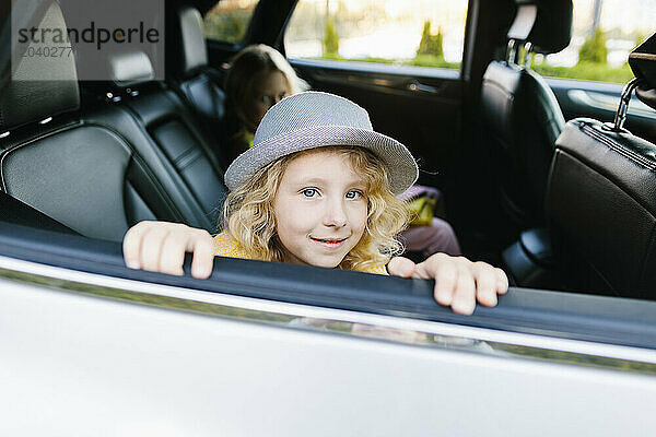 Smiling girl wearing hat and sitting in car with sister