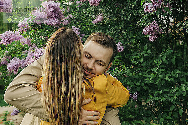 Happy couple hugging each other near lilac tree in park