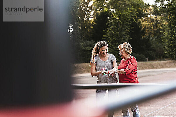 Happy woman examining fitness tracker with grandmother in park