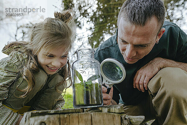 Girl and father looking at plant in glass bottle with magnifying glass