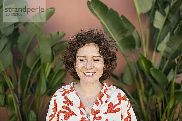 Smiling woman with eyes closed standing in front of wall