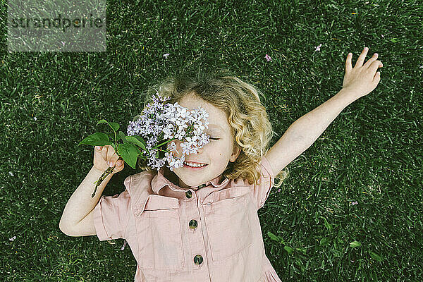 Smiling girl lying on grass with lilac flowers at park