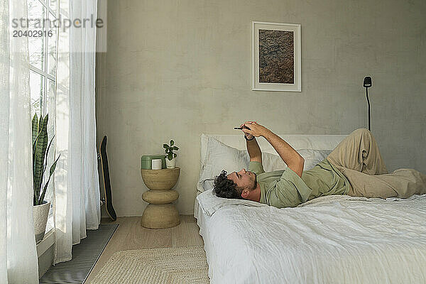 Young man using mobile phone on bed in bedroom at home